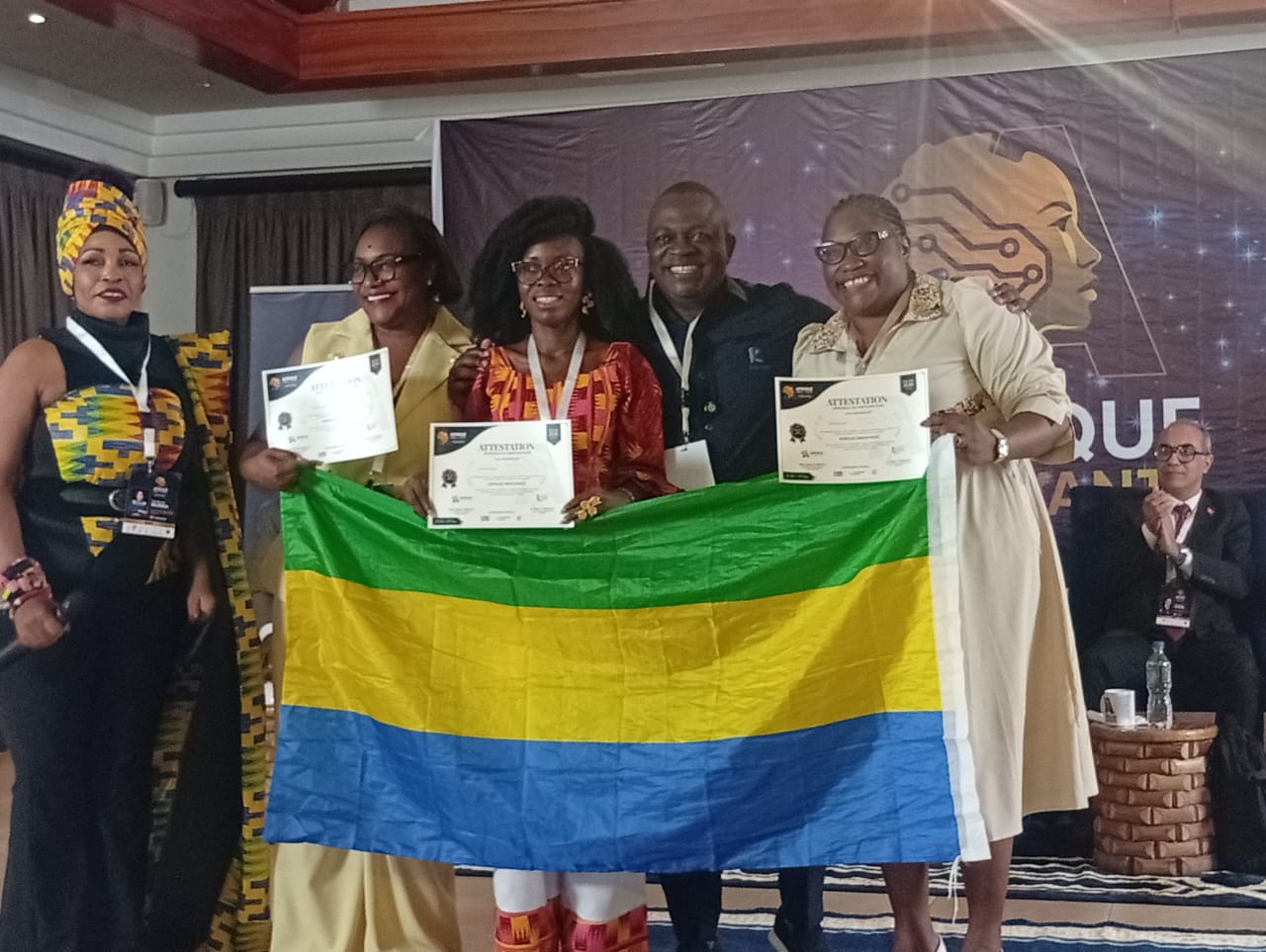 Groupe de lauréates présentant leurs attestations derrière le drapeau gabonais