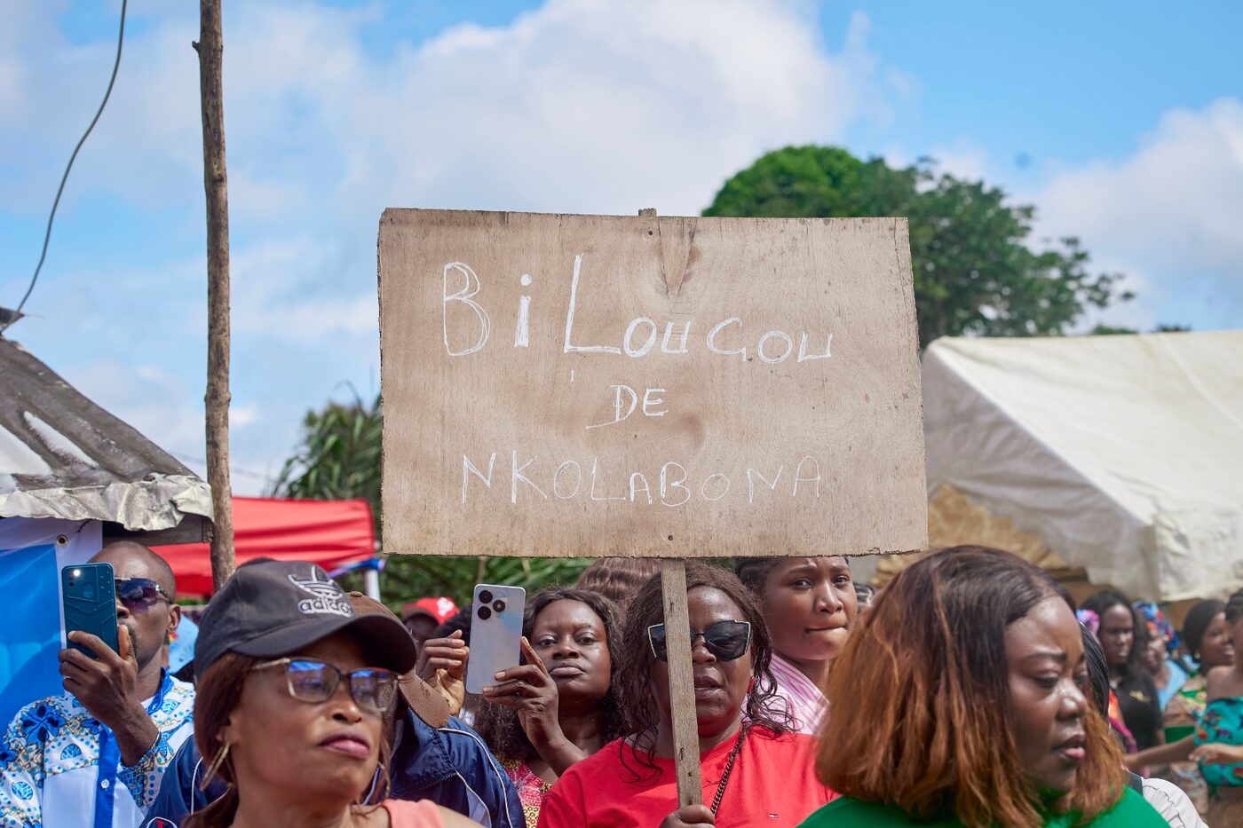 Habitantes derrière une pancarte en bois portant le nom de leur village